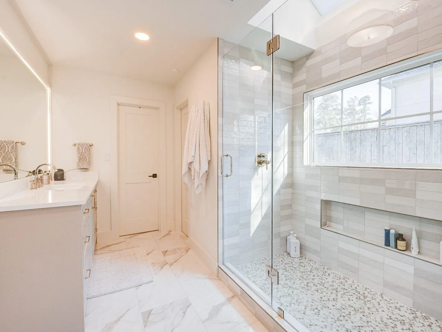 Marble floor tile and a frameless glass shower enclosure in a bathroom remodel in The Woodlands, TX